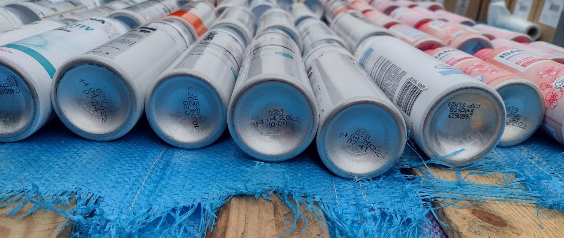 Na drewnianej palecie przykrytej brezentem, rzędy przeterminowanych puszek