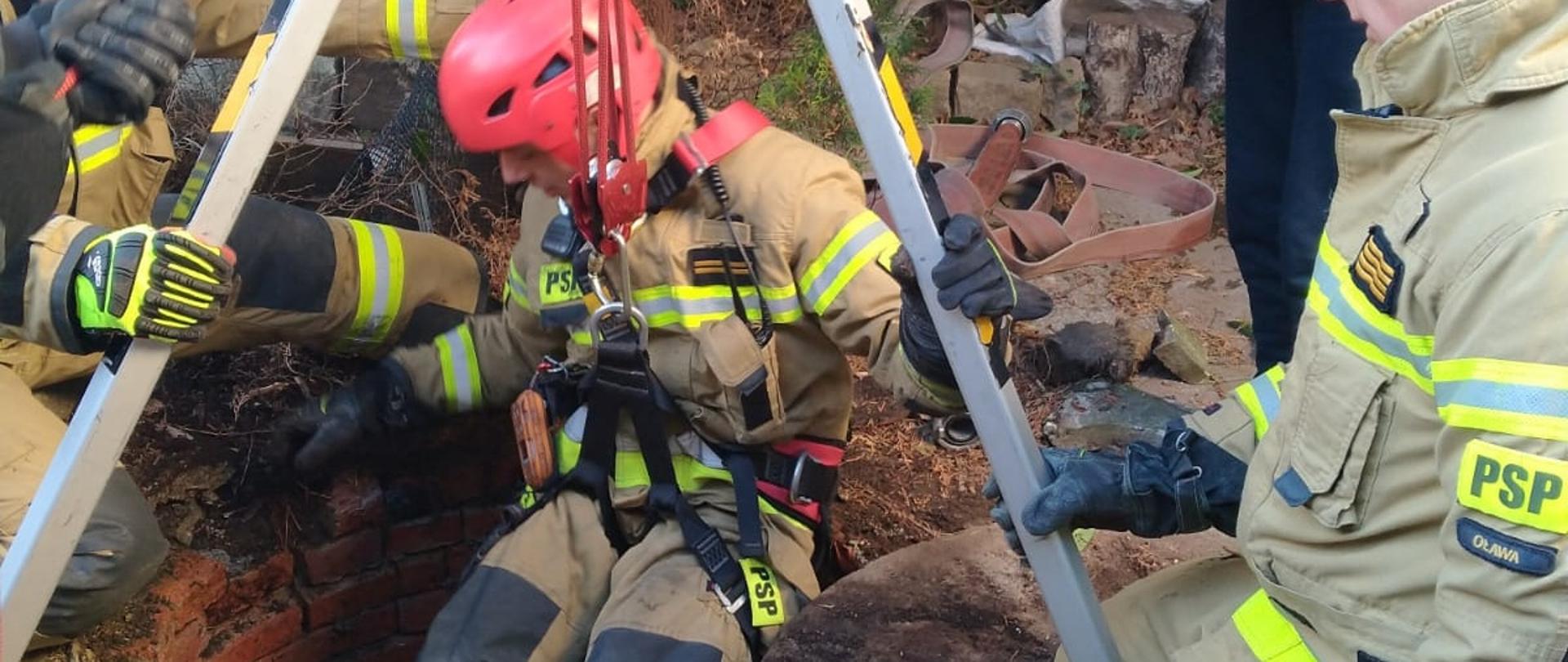 strażak przy użyciu specjalnych zabezpieczeń schodzi na linie do studni