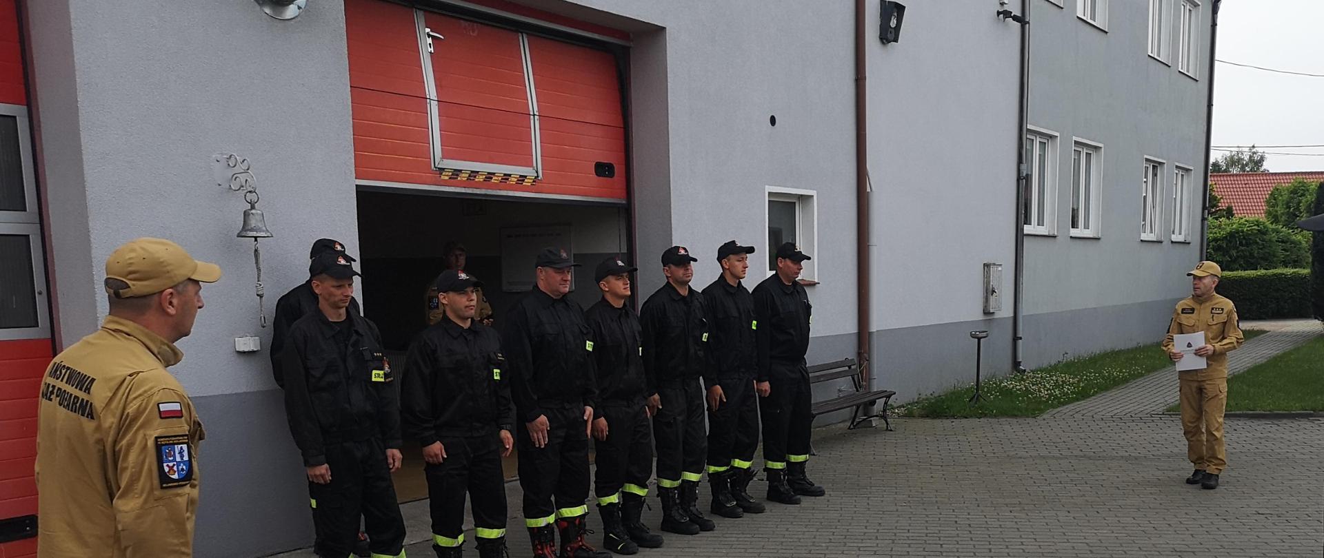 zmiany służbowe podczas uroczystej zmiany służbowej ubrani w mundury koszarowe , po lewej starszy kapitan Robert Liss , po prawej komendant powiatowy państwowej straży pożarnej starszy brygadier Maciej Suchomski ubrani w mundury służbowe z decyzją o przyznaniu nagrody jubileuszowej w rękach