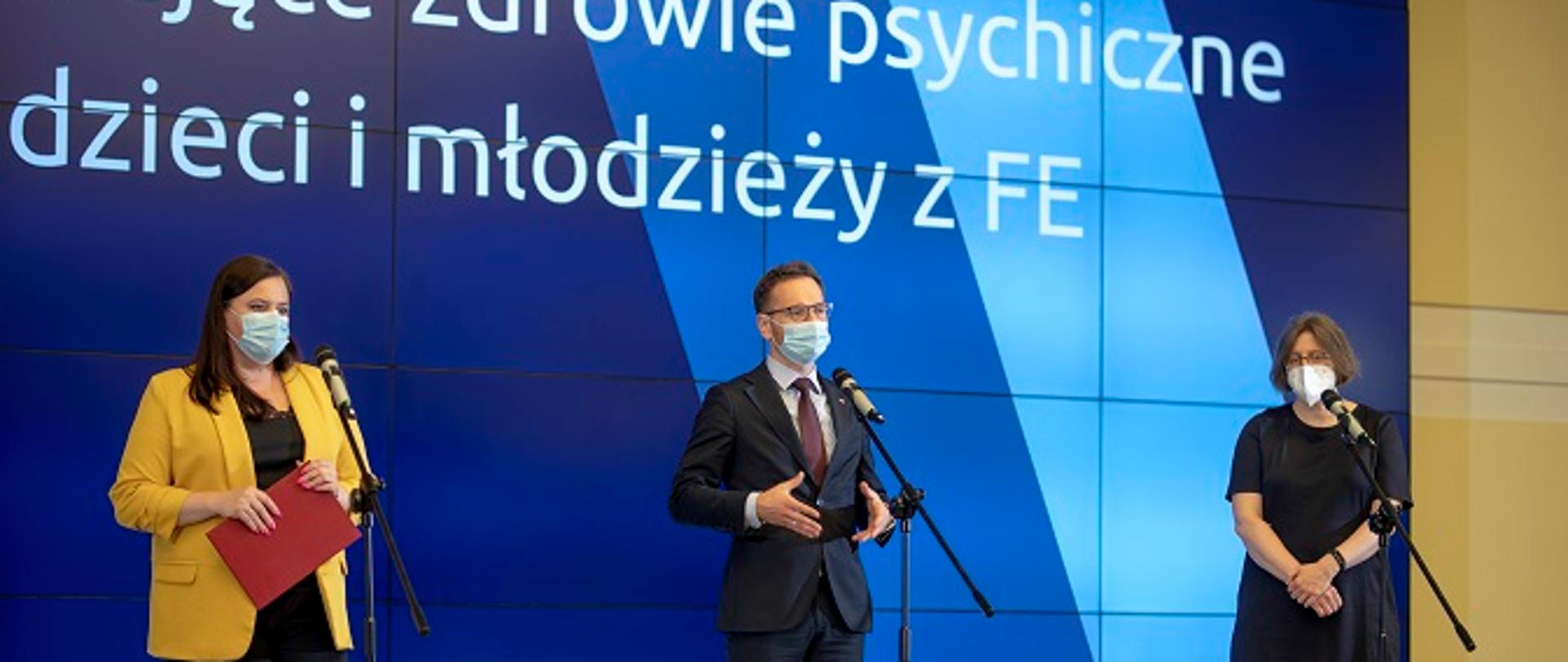 Na scenie przed mikrofonami stoją: wiceminister Małgorzata Jarosińska-Jedynak, wiceminister Waldemar Buda, Małgorzata Remberk, Krajowy Konsultant do spraw zdrowia psychicznego dzieci i młodzieży