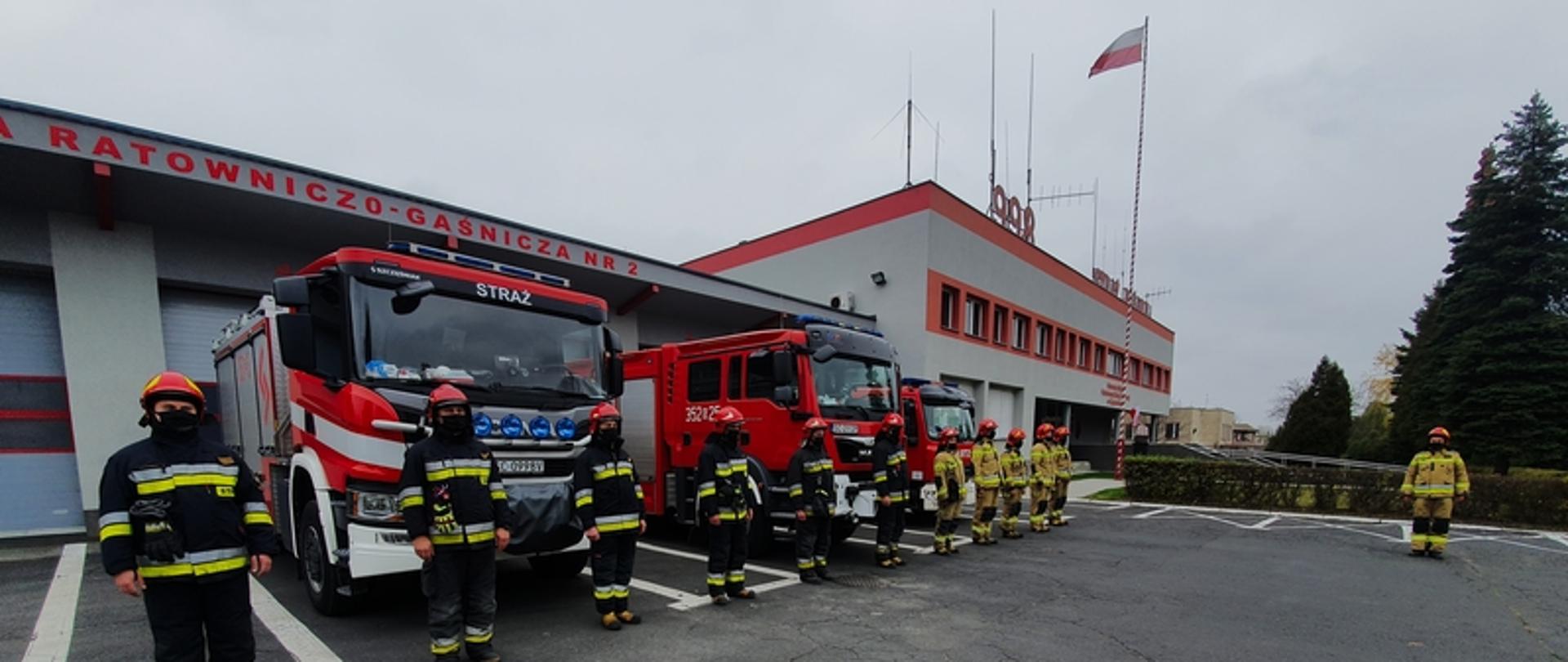 Zdjęcie przedstawia funkcjonariuszy Państwowej Straży Pożarnej podczas obchodów Święta Niepodległości w Jednostce Ratowniczo Gaśniczej nr 2 w Częstochowie. Na zdjęciu widać funkcjonariuszy w umundurowaniu bojowym. Za funkcjonariuszami znajdują się pojazdy bojowe,Jednostki Ratowniczo Gaśniczej nr 2 oraz obiekt Komendy Miejskiej Państwowej Straży Pożarnej w Częstochowie w tle widoczna jest flaga Rzeczypospolitej Polskiej na maszcie. 