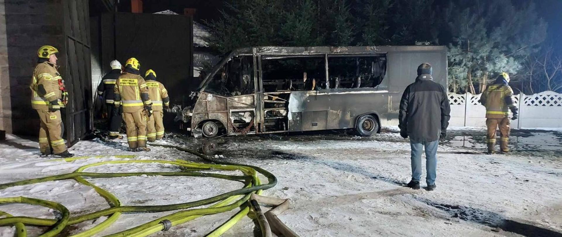 Palony pojazd przed garażem, w pobliżu strażacy