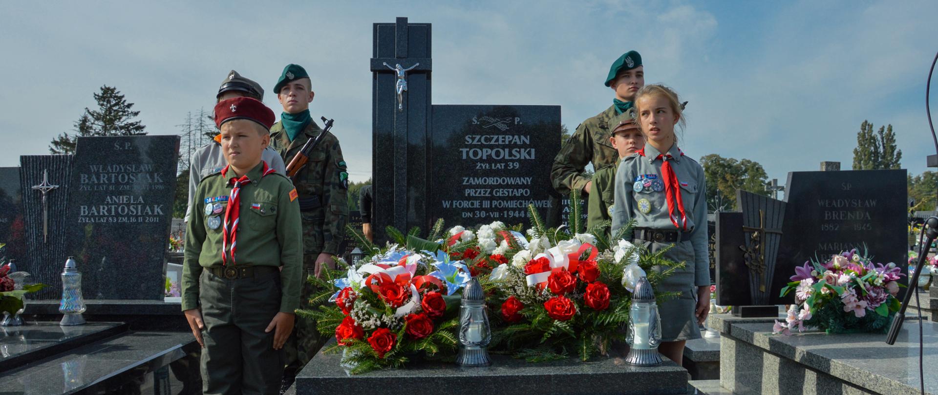 Zdjęcie przedstawia odsłonięty nagrobek Szczepana Topolskiego w Chociszewie. Wartę przy nim pełnią żołnierze i harcerze. Nagrobek udekorowany jest biało-czerwonymi wieńcami oraz zniczami