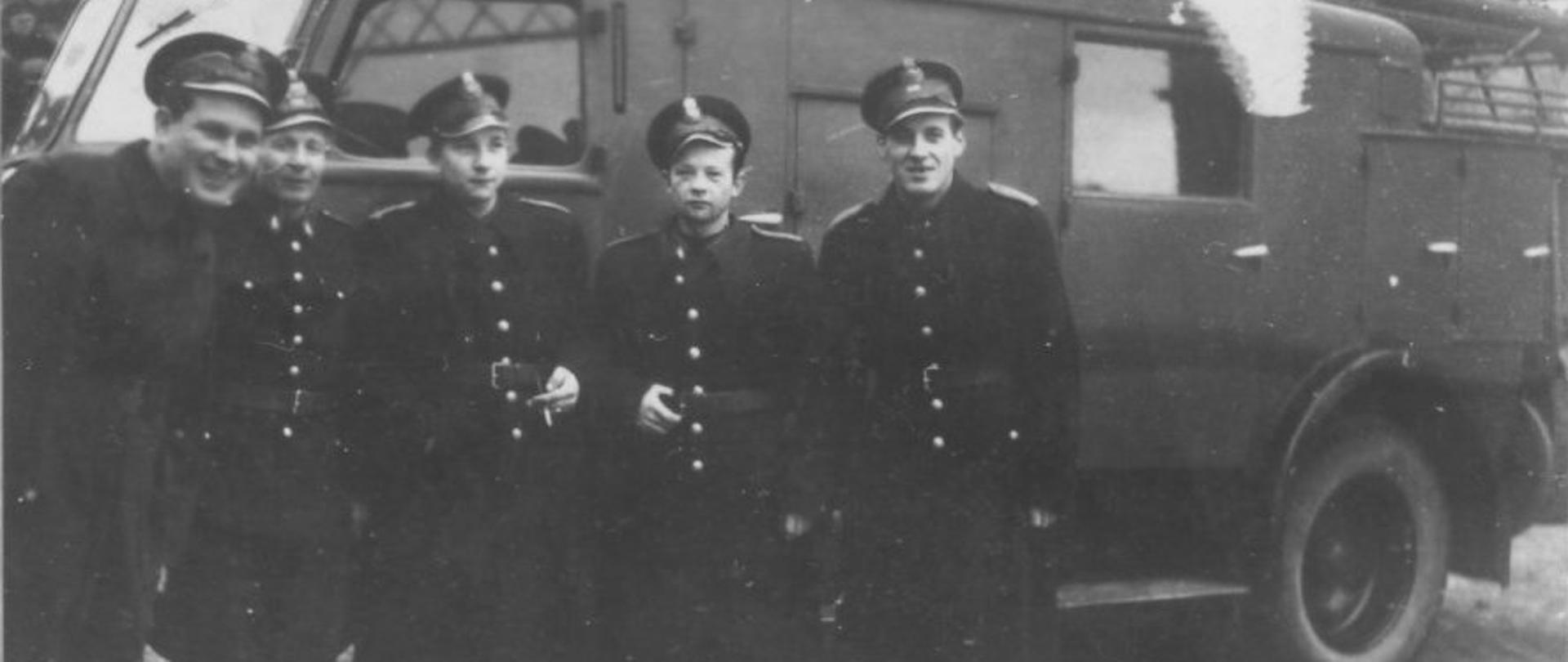 Stare czarno białe zdjęcie.Strażacy w mundurach przy samochodzie pożarniczym. 
