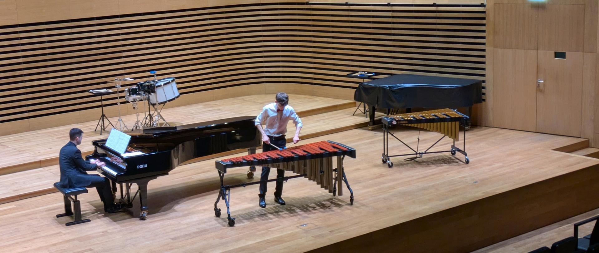 Chłopak gra na marimbie, mężczyzna akomoaniuje na fortepianie.