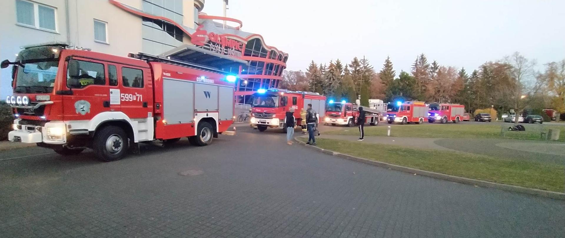 Widać pięć samochodów strażacki przed budynkiem hotel, po prawej jest trawnik