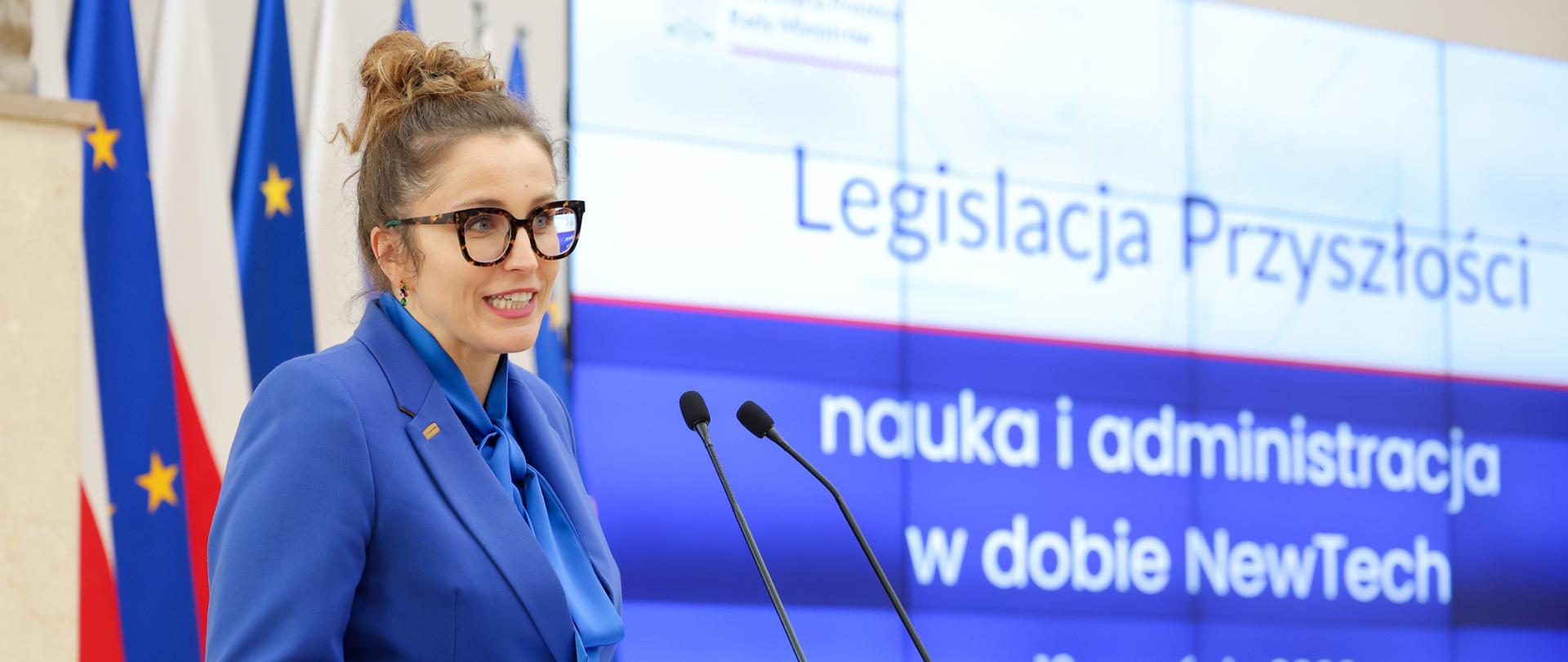 zdjęcie przedstawia Koordynator ds. Oceny Skutków Regulacji Katarzynę Grzelak-Bach na tle flag Polski i Unii Europejskiej