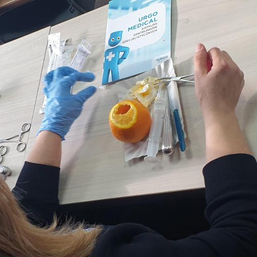 Na stole oprócz pomarańczy znajdują się materiały opatrunkowe oraz katalog opatrunków specjalistycznych. Do tego kilka par nożyczek.