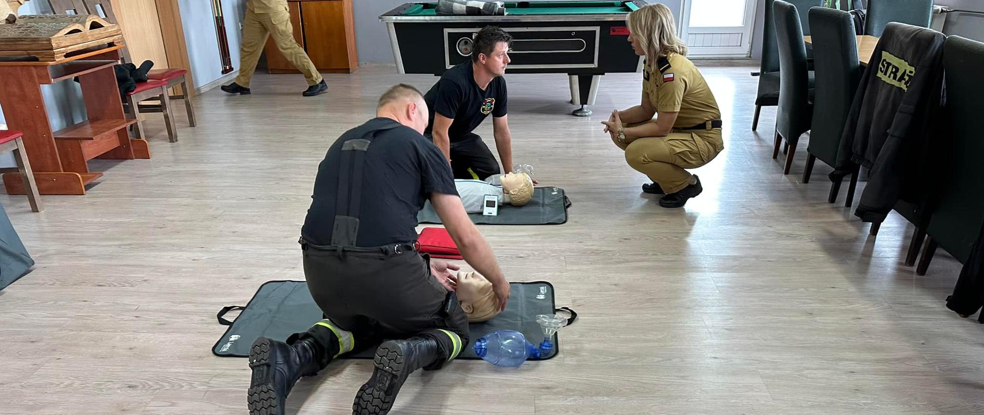 Na zdjęciu znajdują się strażacy którzy klęczą przy fantomach do udzielania KPP obok nich przyklęka strażaczka