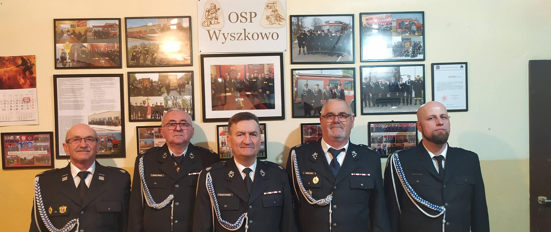 Na zdjęciu pięciu strażaków ochotników w mundurach galowych. W tle ścianka z pamiątkowymi zdjęciami życia jednostki.