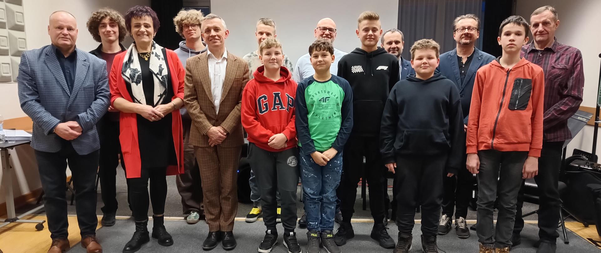 Uczniowie, nauczyciele i wykładowcy stoją w grupie.