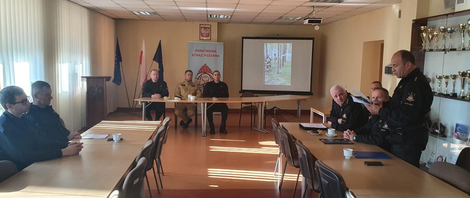 Zdjęcie obrazuje podsumowanie ćwiczeń powiatowych pod kryptonimem "Lasy 2021". W podsumowaniu ćwiczeń uczestniczyli- naczelnik Wydziału Operacyjnego Komendy Wojewódzkiej PSP w Kielcach bryg. Marcin Nyga, komendant powiatowy PSP w Jędrzejowie st. bryg. Paweł Jakubowski wraz z zastępcą bryg. Tomaszem Szymańskim oraz rozjemcy, którzy oceniali ćwiczenia. Na zdjęciu głos zabiera główny rozjemca ćwiczeń.