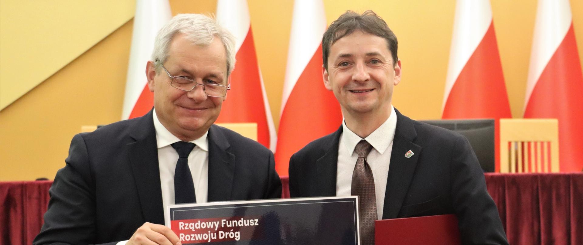 Mężczyźni trzymający czek na tle flag 