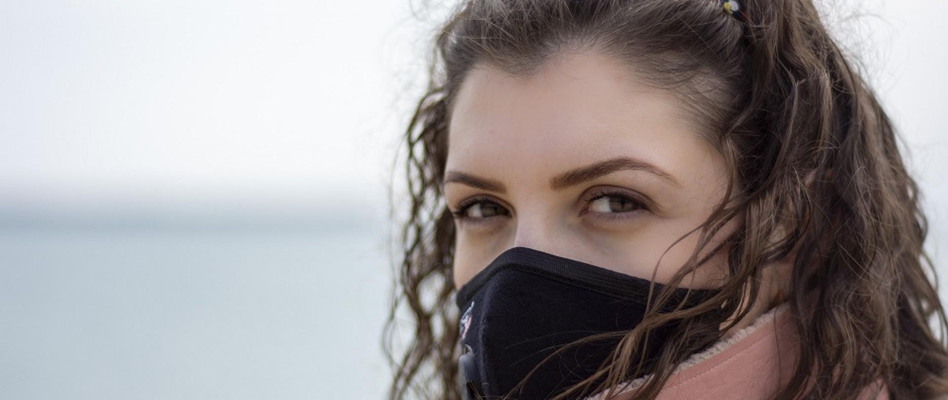 Twarz kobiety z ochronną maseczką wielorazową na twarzy. Kobieta jest na zewnątrz, ubrana w ciepłą kurtkę