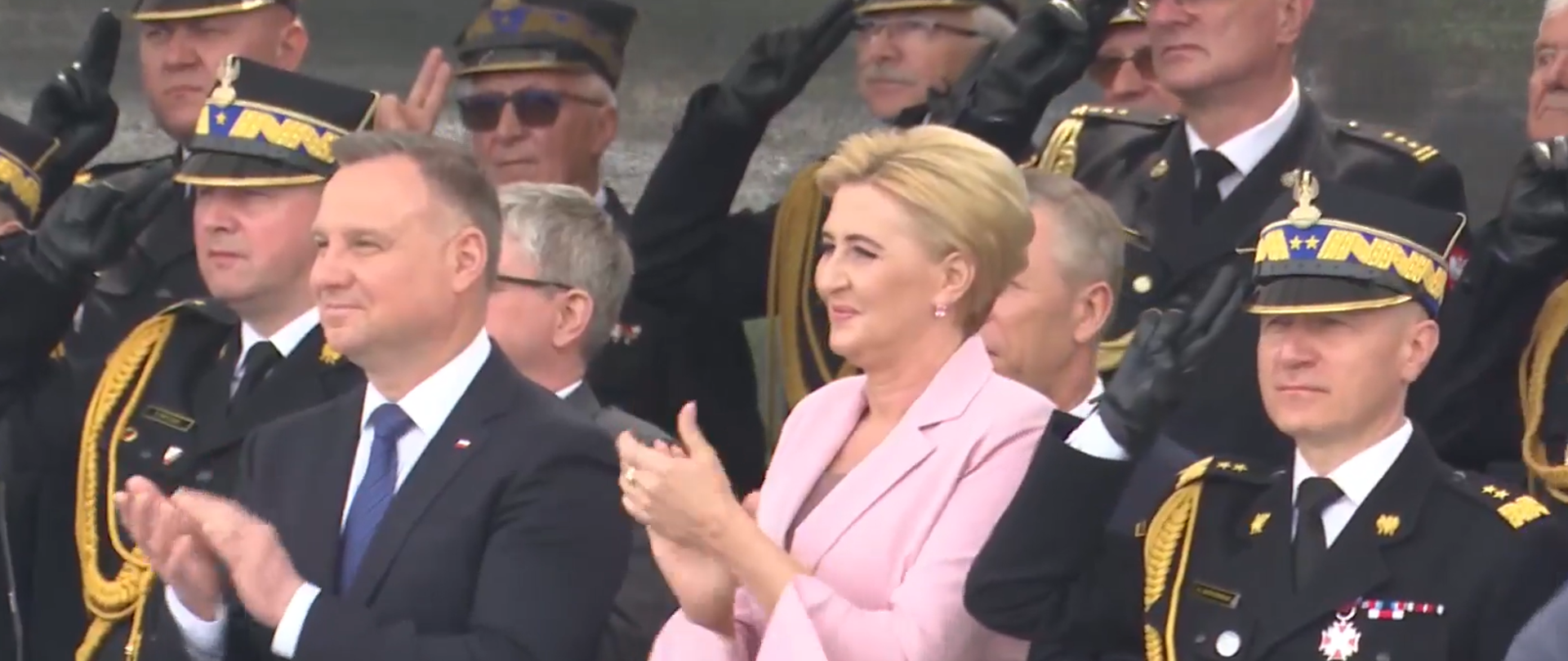 grupa strażaków z prezydentem Dudą i jego żoną na czele , strażacy salutują, osoby cywilne klaszczą