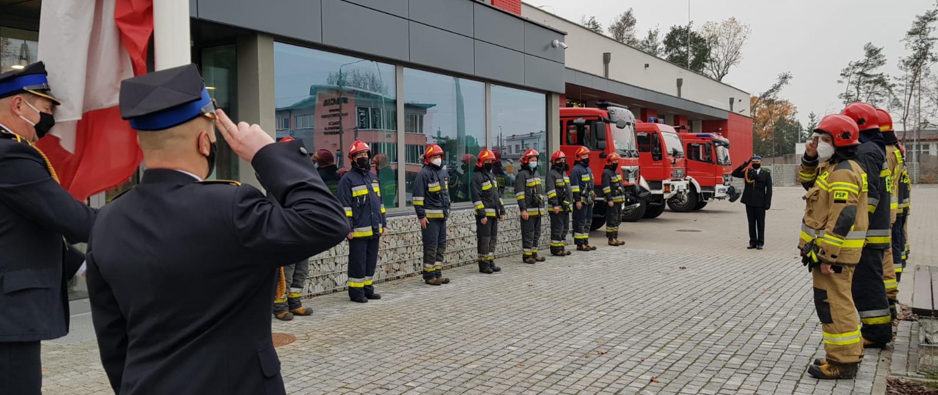 Uroczysta zmiana służby z podniesieniem Flagi Państwowej z okazji Święta Niepodległości
Przed budynkiem KP PSP w Legionowie funkcjonariusze podczas podnoszenia flagi wszyscy oddają honor przez salutowanie. Przodem do masztu dowódca uroczystości bokiem po obu stronach zmiany służbowe za masztem poczet flagowy.