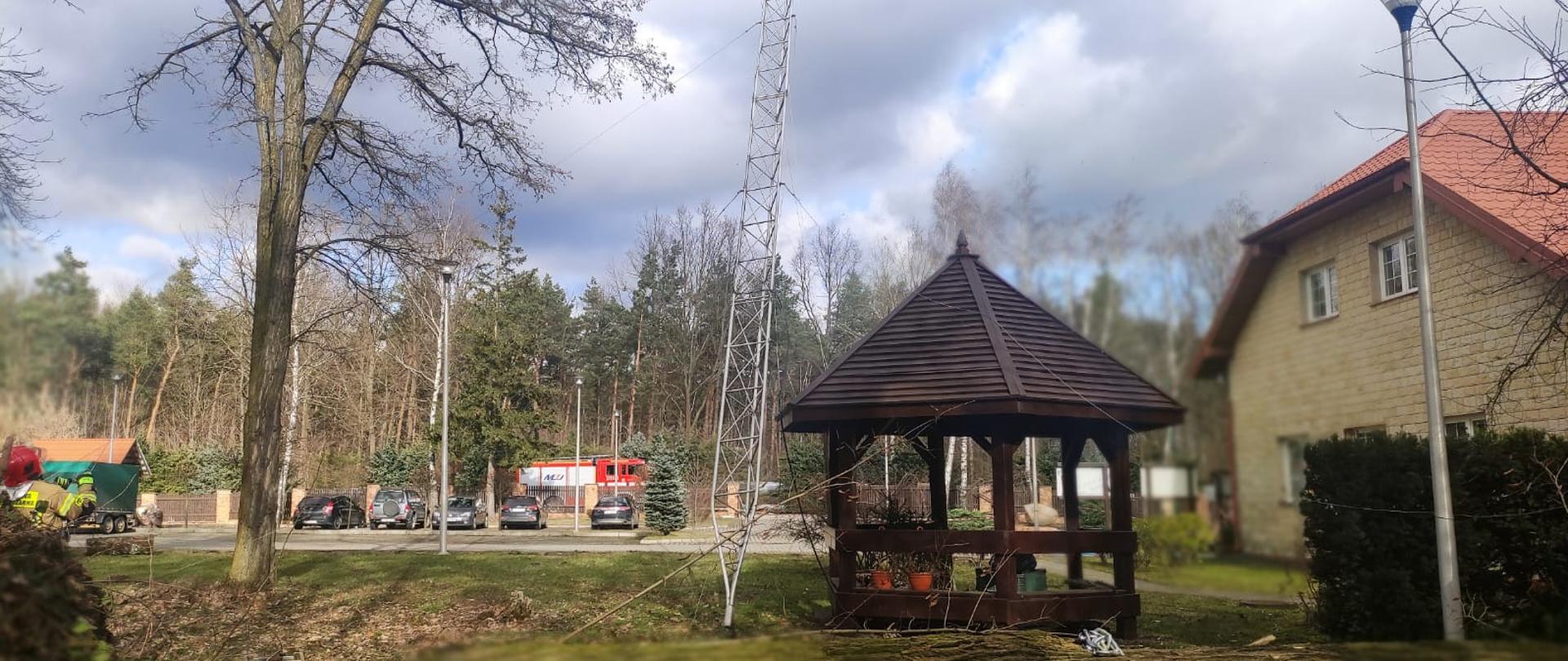 Zdjęcie przedstawia teren Nadleśnictwa Kielce i aluminiowy maszt niebezpiecznie pochylony. Przy nim stoi altanka rekreacyjna, a prawej strony budynek Nadleśnictwa Kielce.