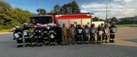 Zdjęcie grupowe po zakończonym egzaminie grupa strażaków stoi na tle wozu ratowniczo-gaśniczego