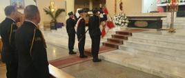 Zdjęcie przedstawia strażaków stojących w kościele. Trzech strażaków stoi ze sztandarem, dwóch stoi w ławce. 