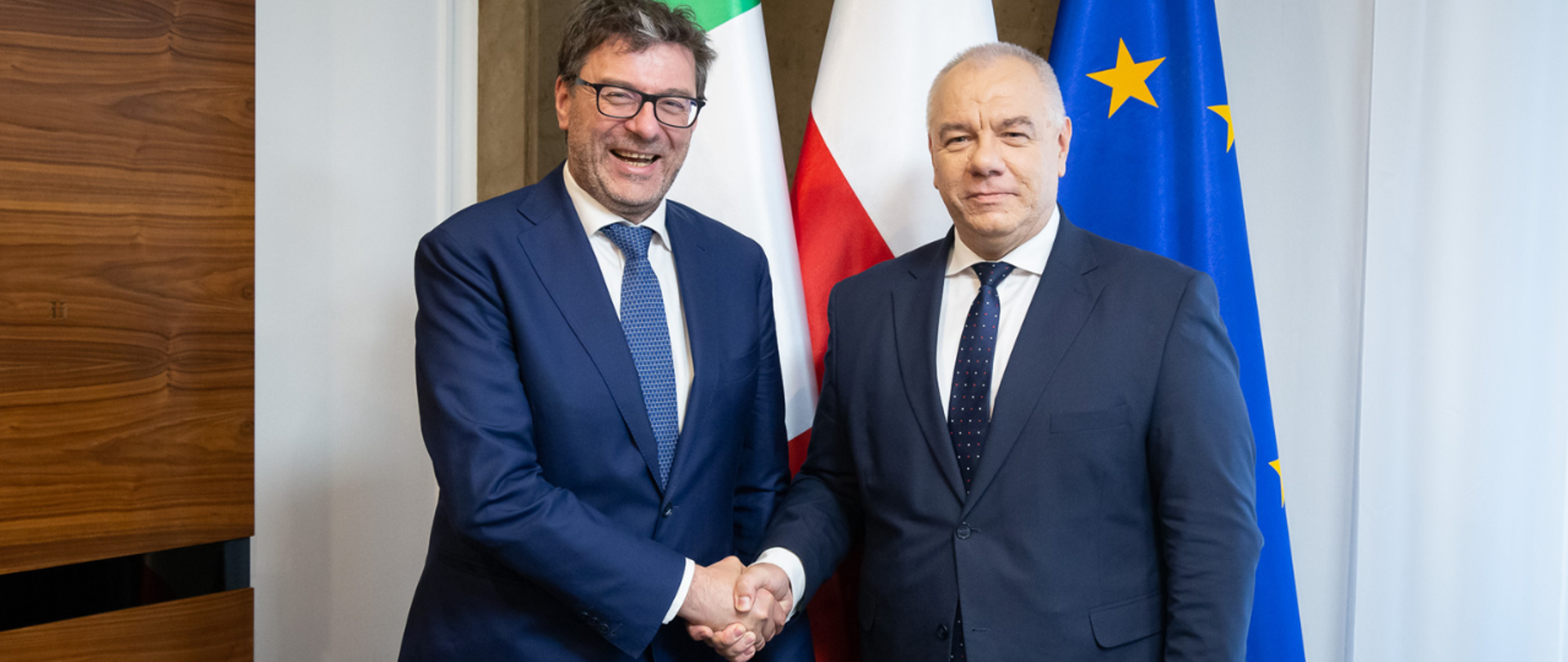 Wicepremier Jacek Sasin i minister rozwoju gospodarczego Włoch Giancarlo Giorgetti pozują do wspólnego zdjęcia na tle flag: włoskiej, polskiej i unijnej