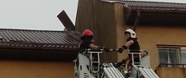 Dwóch strażaków w koszu drabiny mechanicznej przy uszkodzonej obróbce dachu na budynku mieszkalnym 