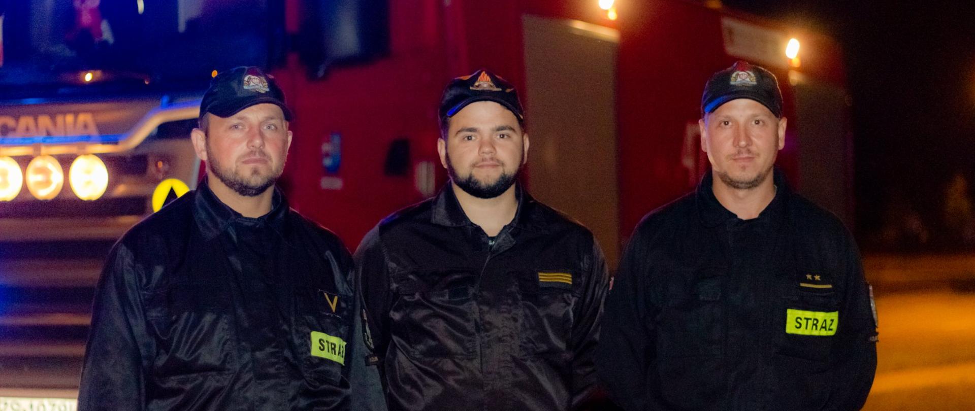 Trzech strażaków na tle samochodu gaśniczego