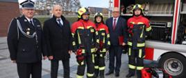 Minister Rozwoju i Technologii Pan Grzegorz Piechowiak, Pan Igor Kołoszuk Burmistrz Miasta Obrzycko, druh Zbigniew Wleklak Prezes OSP Obrzycko oraz trzech członków OSP w mundurach specjalnych podczas wręczania sprzętu dla jednostki OSP Obrzycko.