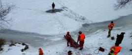 Widok z lotu ptaka na miejsce prowadzonych ćwiczeń na zamarzniętym akwenie wodnym. Widoczni strażacy ćwiczący na lodzie.