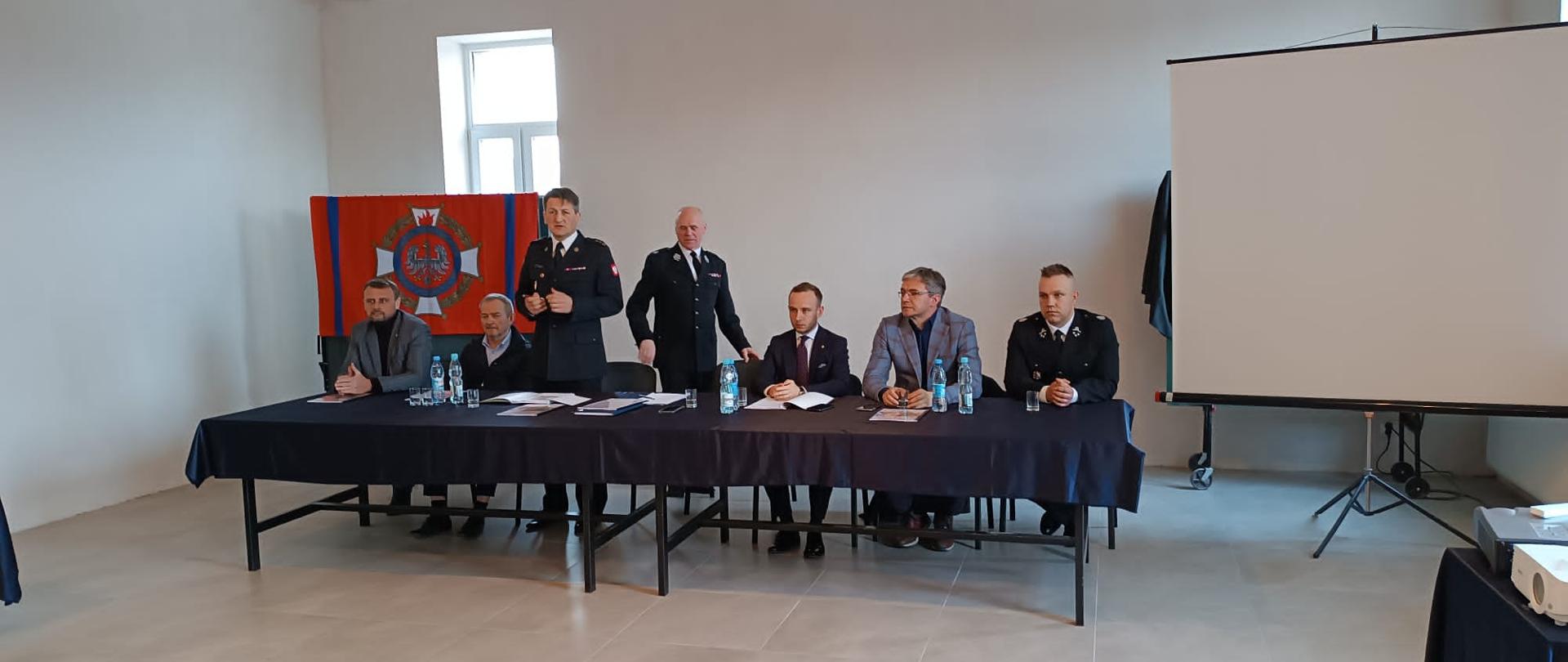 Zdjęcie przedstawia gości i organizatorów spotkania sprawozdawczego Ochotniczej Straży Pożarnej w Ćmińsku. Głos zabiera bryg. Mariusz Góra – komendant miejski PSP w Kielcach