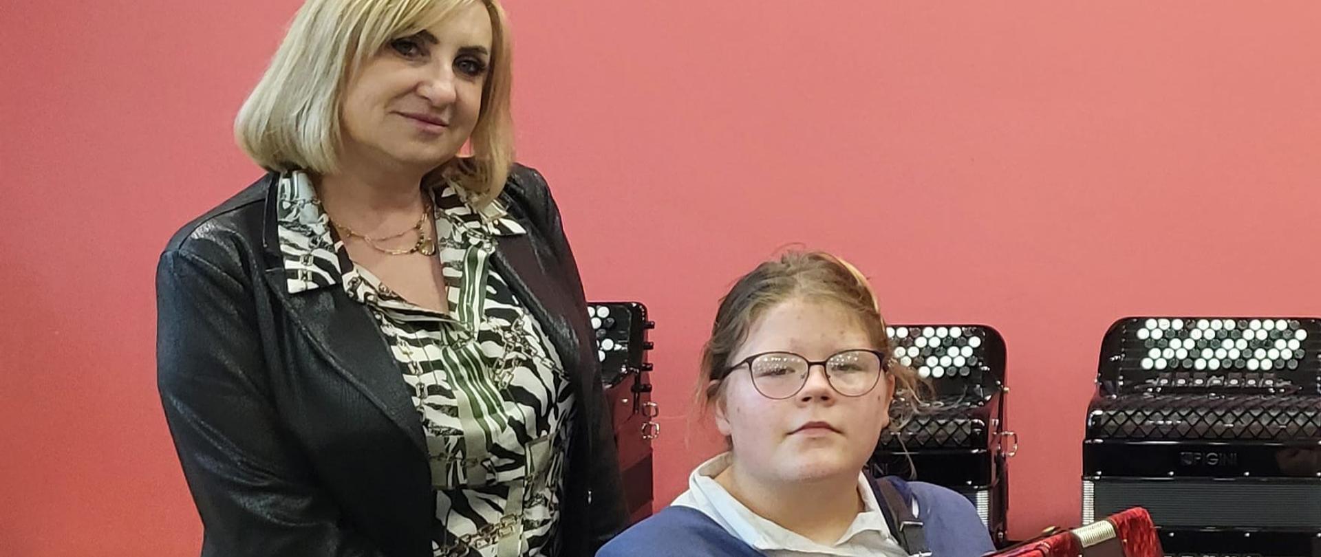 Zdjęcie - siedząca na krześle z akordeonem Zuzanna Wąs ze stojącą obok swoją nauczycielką Ewą Rudzką-Sługocką