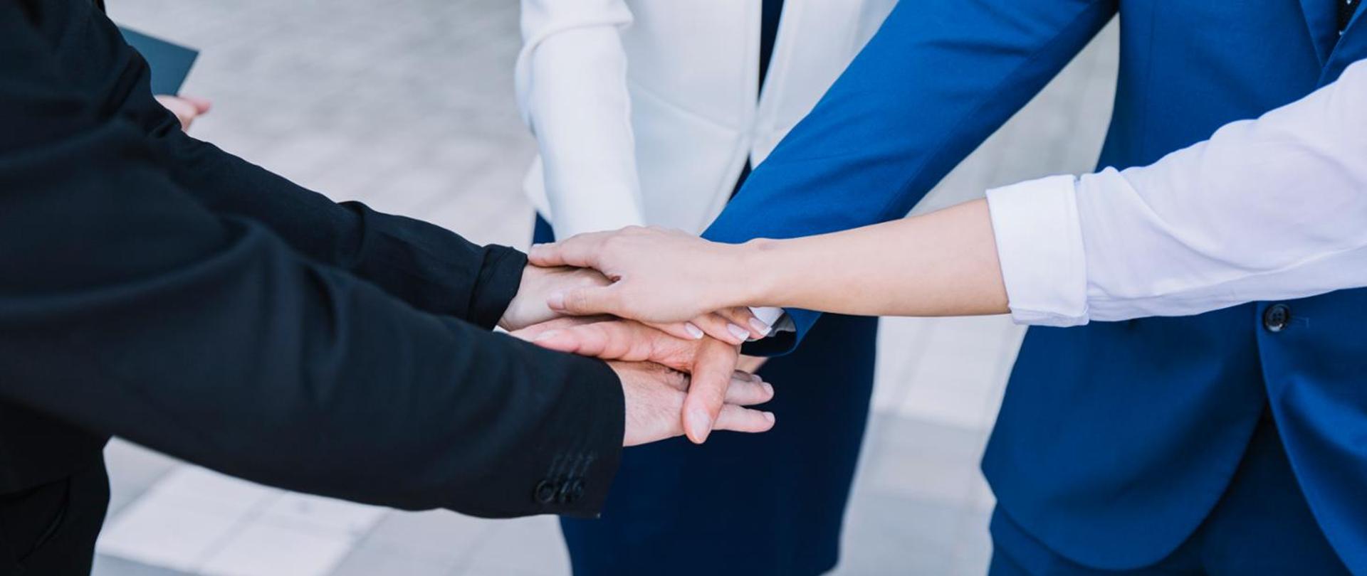 dłonie osób ułożone jedna na drugiej symbolizujące współpracę