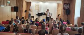 Zdjęcie przedstawia Koncert rekrutacyjny w sali koncertowej szkoły od strony widowni, na scenie prezentacja puzonu