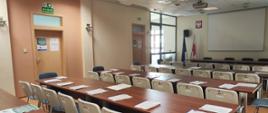 Sala konferencyjna przygotowana do szkolenia, materiały szkoleniowe na stołach.