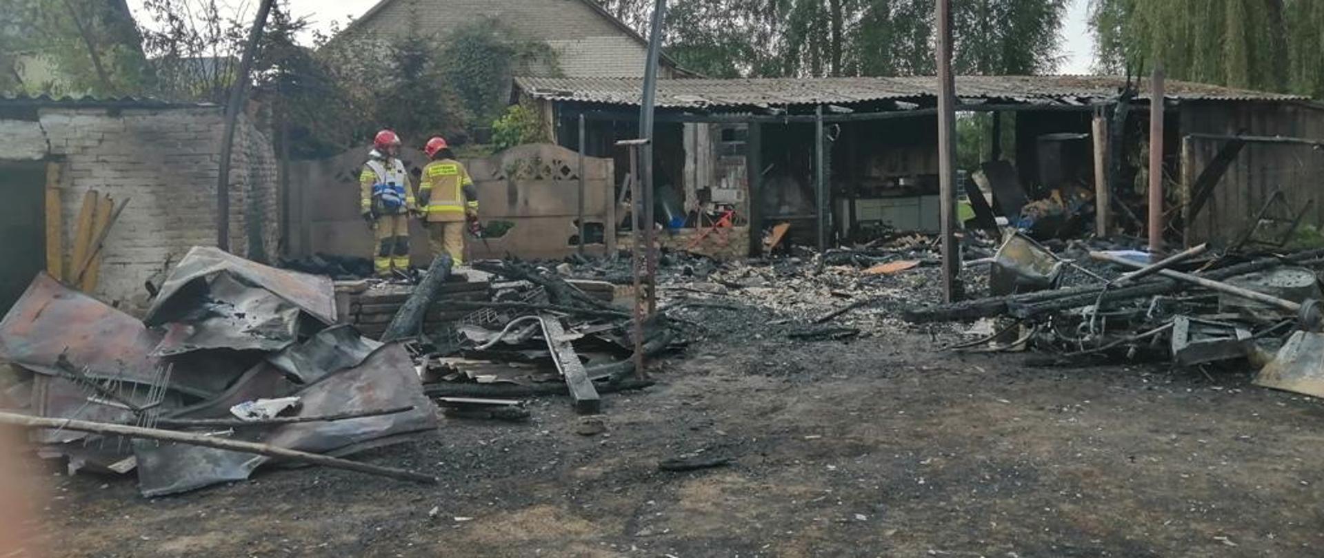 Na zdjęciu spalone budynki gospodarcze oraz dwóch strażaków w ubraniach specjalnych prowadzących działania