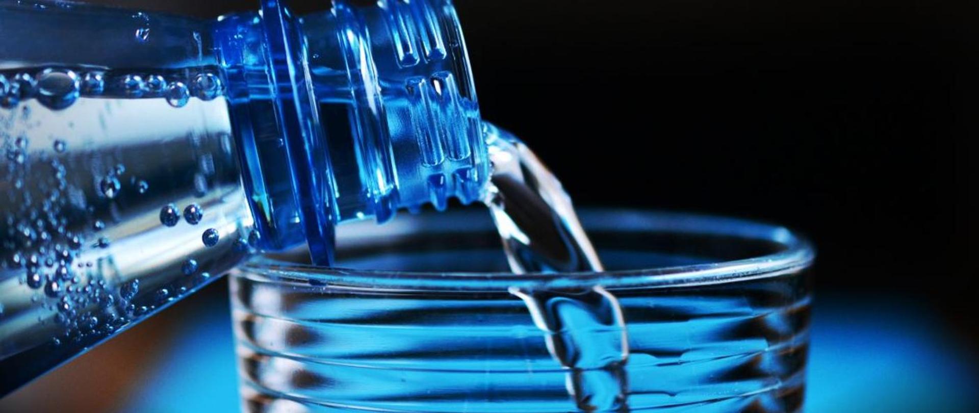 szklanka wody do której wlewana jest woda mineralna z butelki