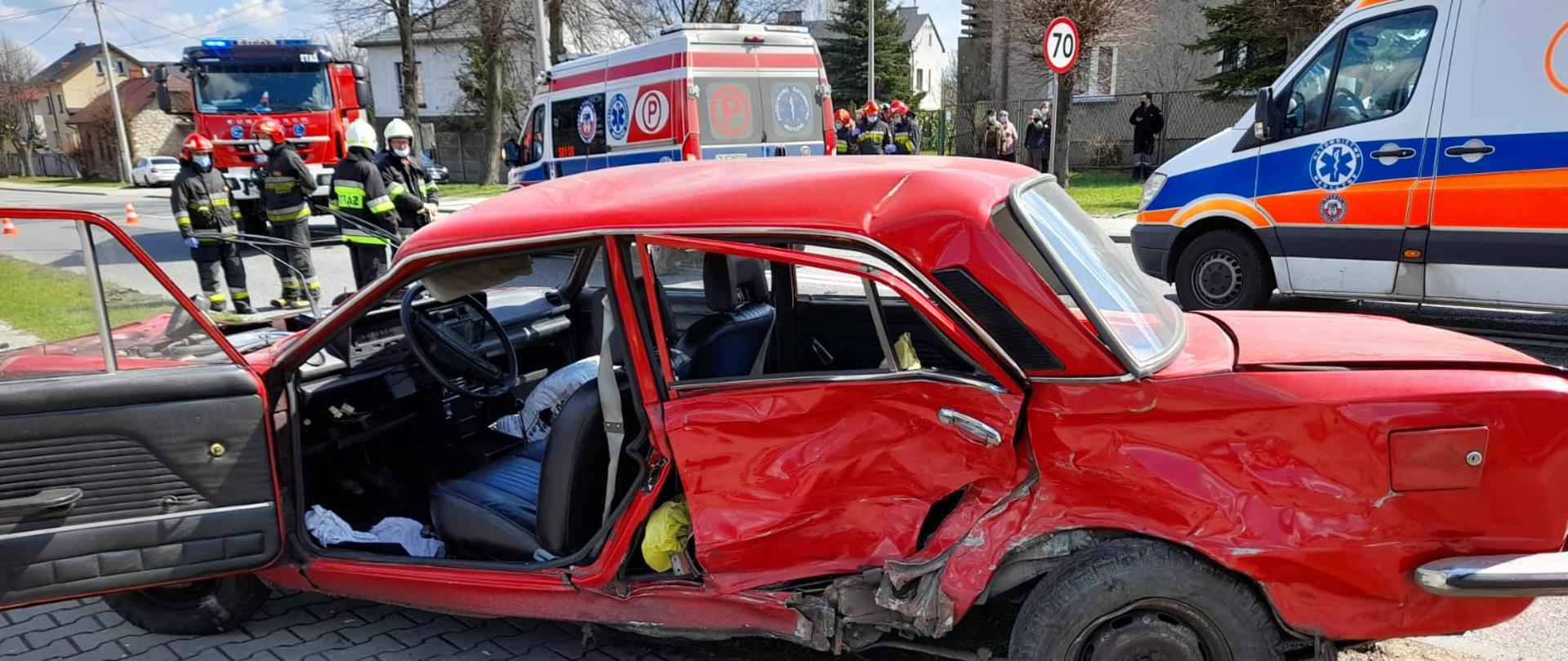 Zdjęcie przedstawia pojazd po wypadku drogowym w tle widać pojazdy pożarnicze oraz Pogotowie oraz strażaków