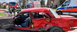 Zdjęcie przedstawia pojazd po wypadku drogowym w tle widać pojazdy pożarnicze oraz Pogotowie oraz strażaków