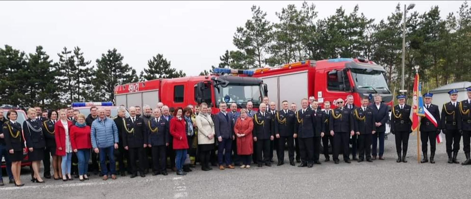 Zdjęcie przedstawia osoby na tle samochodów pożarniczych