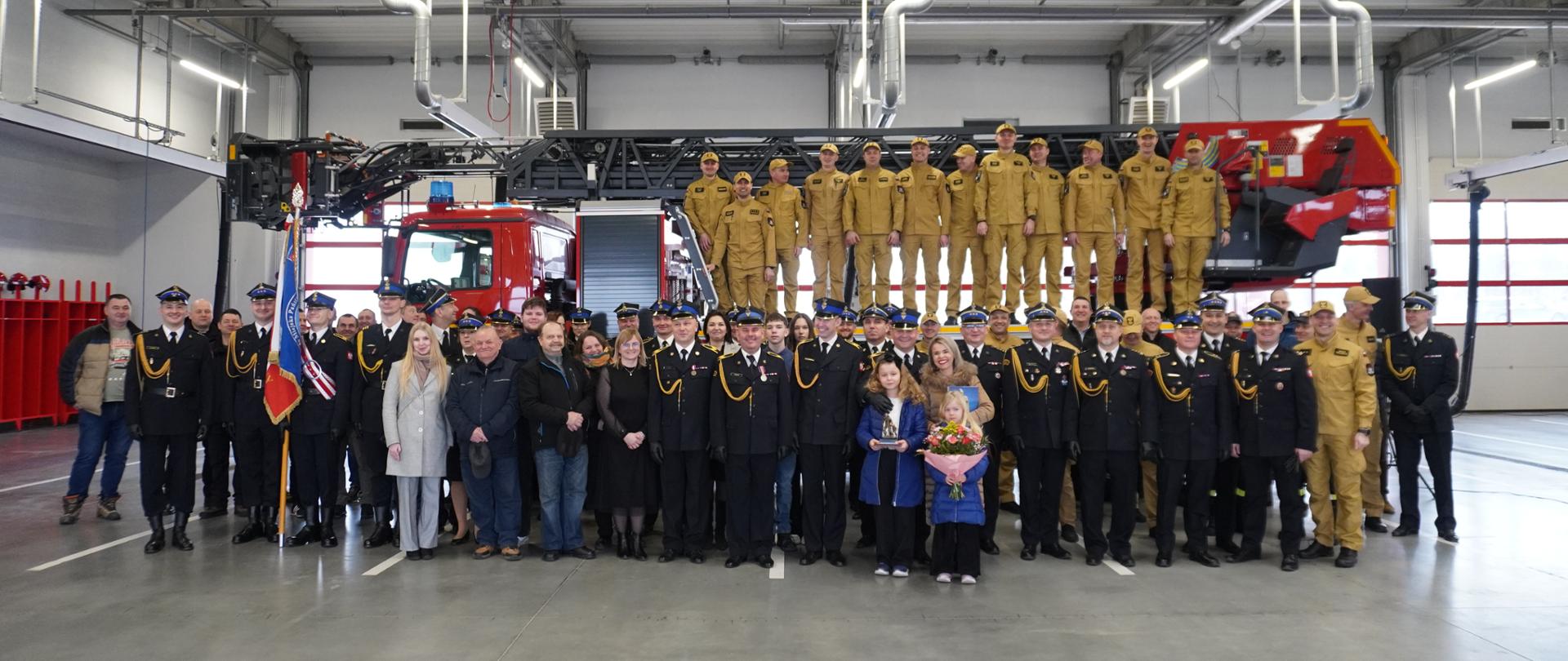 Zdjęcie grupowe strażaków PSP oraz gości na terenie JRG 3 w Rzeszowie, z drabiną mechaniczną w tle.