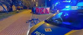 Na pierwszym planie radiowóz Policji, w tle parawan straży pożarnej i uszkodzony rower