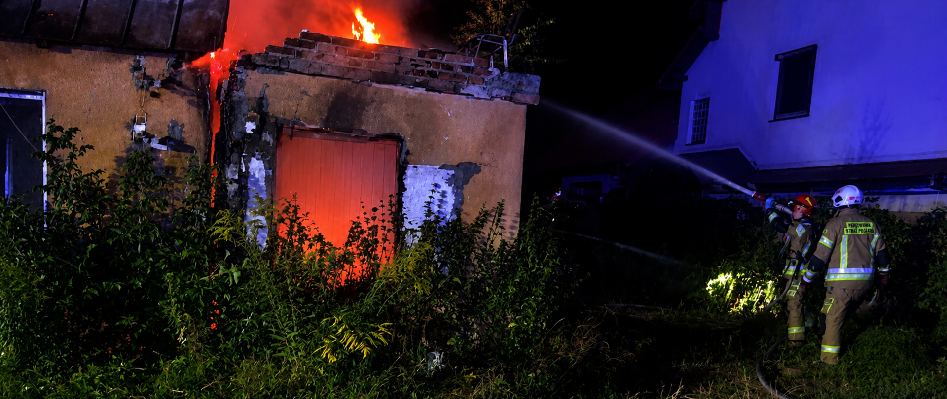 Fotografia przedstawia strażaków gaszących nocny pożar budynku jednorodzinnego