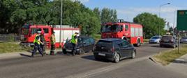 Zdjęcie przedstawia miejsce wypadku na ulicy Połczyńskiej w Białogardzie. W tle dwa pojazdy strażackie, a przed nimi na drodze uszkodzony samochód Renault Clio. Przed pojazdem strażacy i policjanci