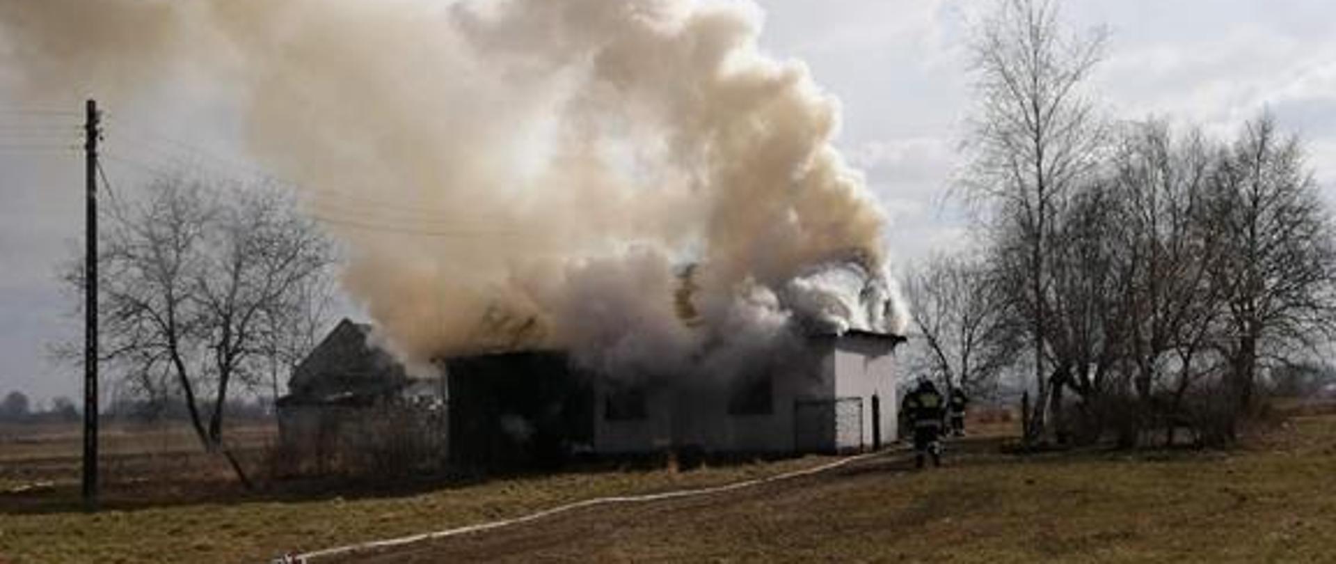 Pożar budynku mieszkalnego, strażacy rozwijają linię gaśniczą w kierunku pożaru, prowadzą działania gaśnicze.