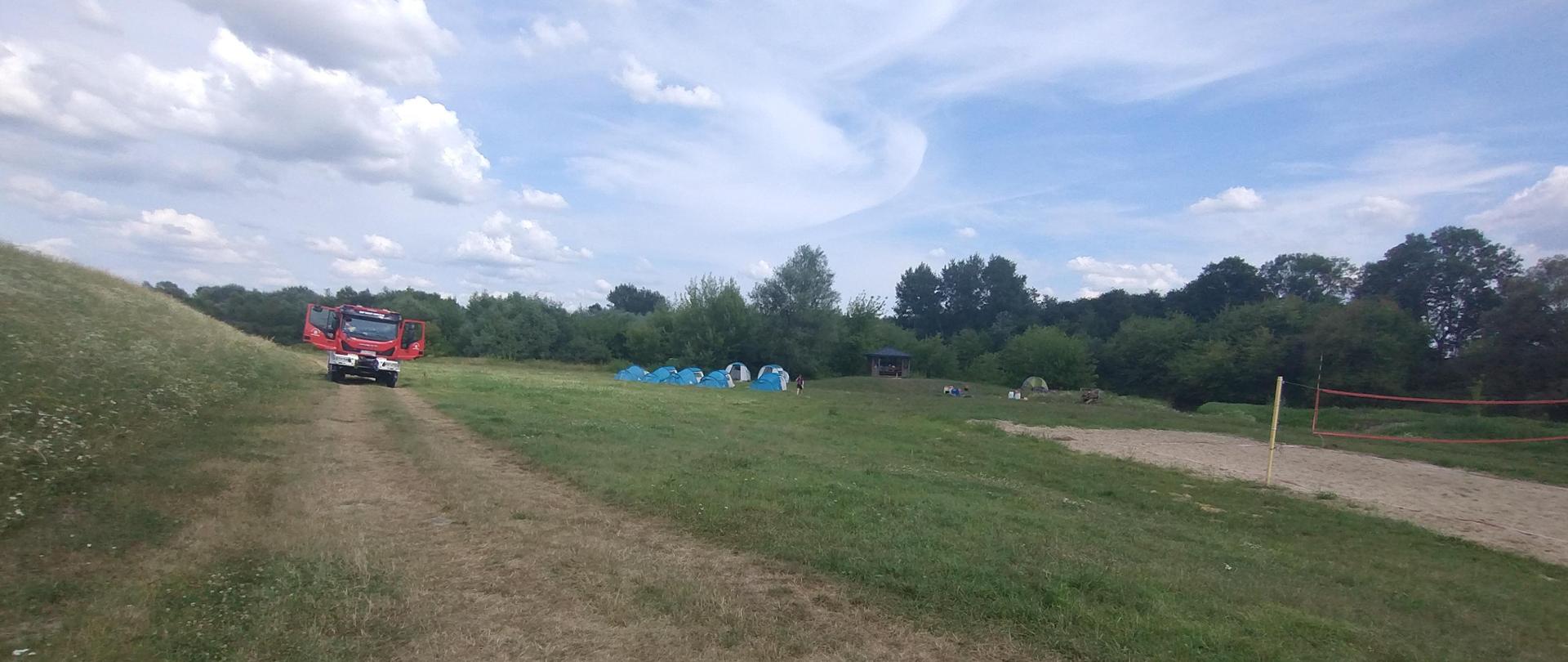 Na 1 planie trawa. w tle namioty i samochód stojący i drzewa.