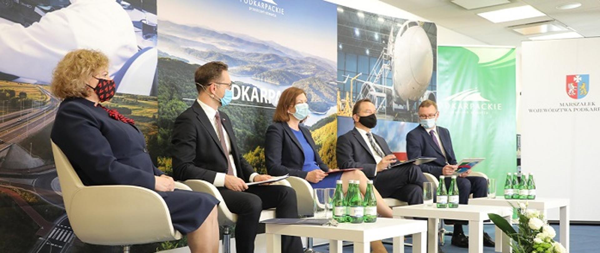 Pięć osób, dwie kobiety, trzech mężczyzn, siedzą w rzędzie na konferencji. Za nimi zdjęcia przedstawiające krajobraz Podkarpacia.