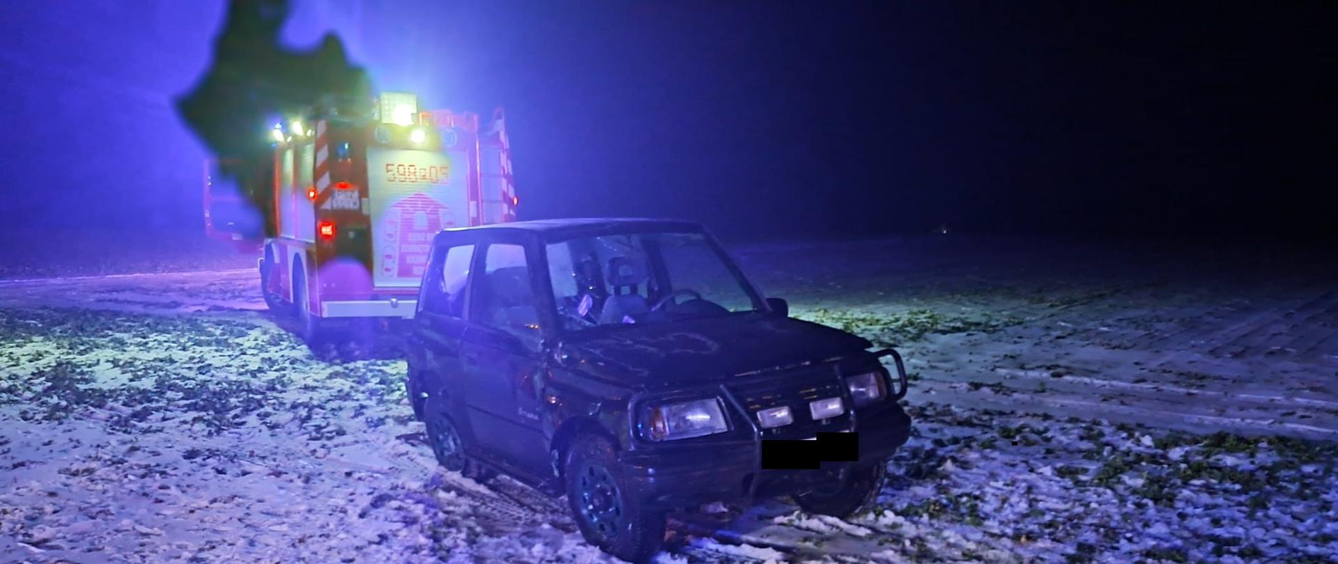 Uszkodzony samochód i pojazd strażacki na polu, jest noc