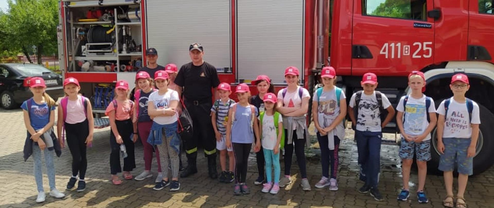 Zdjęcie grupowe dzieci z dwoma strażakami na tle wozu ratowniczo-gaśniczego