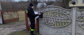 Strażak wrzuca ulotkę do skrzynki na listy znajdującej się na ogrodzeniu posesji 