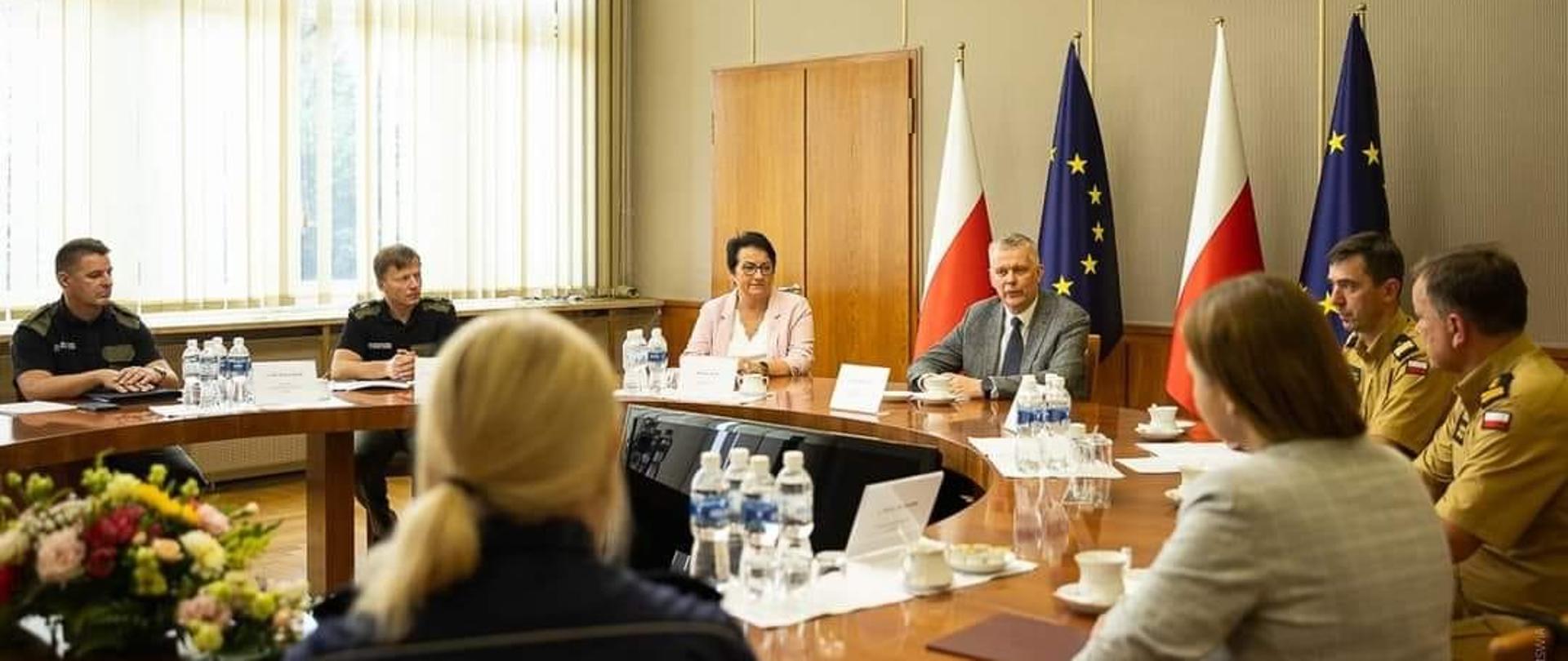 Na zdjęciu Wojewoda Opolski Monika Jurek, Minister Tomasz Siemoniak oraz pozostali uczestnicy spotkania siedzą przy okrągłym stole w Sali Złotej. 