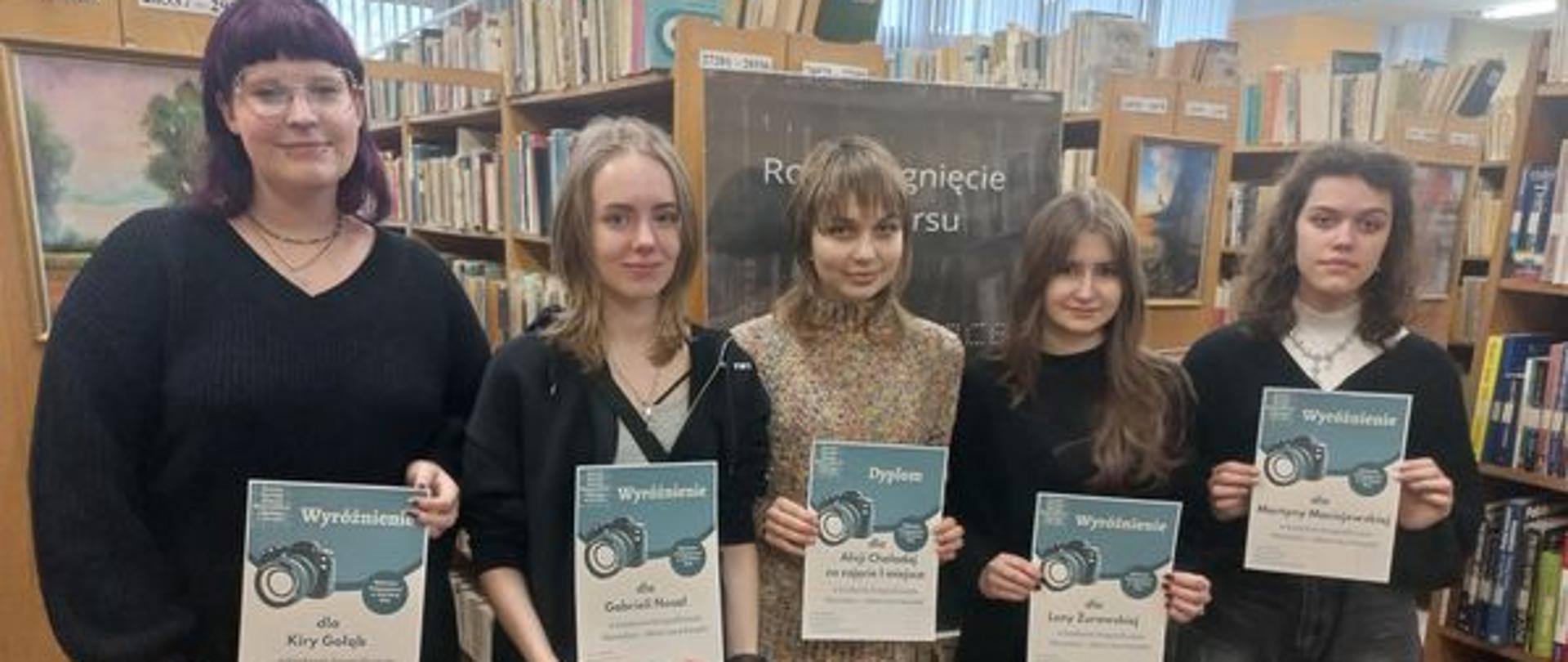 Na zdjęciu uczennice PLSP, laureatki konkursu „Sleeveface - ubierz się w książkę”, z dyplomami na tle regałów z książkami w Bibliotece Pedagogicznej w Zduńskiej Woli.